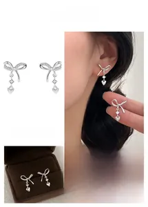 Detail of silver bow earrings with heart charm, cubic zirconia inlay and gift box