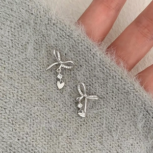 Silver bow earrings with heart zircon pendants on a gray knit fabric backdrop