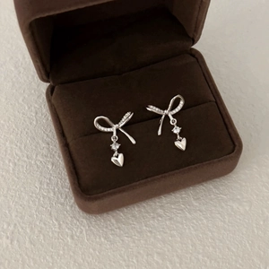 Elegant silver bow earrings with zircon heart pendants on a brown velvet jewelry box