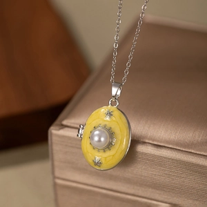 Detail of opening oval locket necklace with yellow enamel, pearl, and silver star pattern