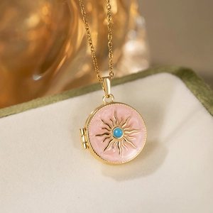 Macro view of a vintage round pink enamel locket necklace with gold sunburst and blue bead