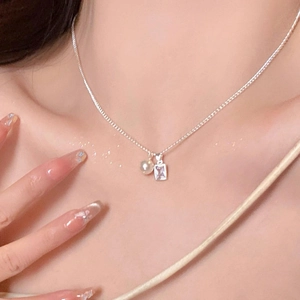 Close-up of a silver necklace featuring heart and square zircon pendants on a collarbone