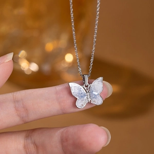 Macro shot of silver butterfly necklace with zircon and pearl inlay held on fingertips