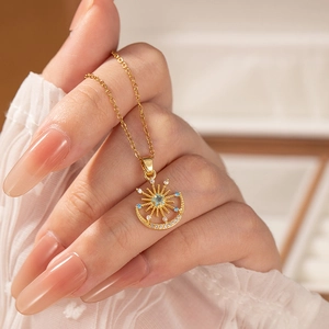 Collier élégant soleil et lune en or avec pierre étoile bleue porté par une main en dentelle