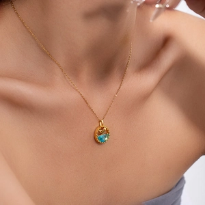 Golden mermaid tail necklace with a blue round gemstone pendant shown on a model