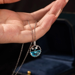 Macro detail of silver fishtail pendant with blue gemstone held in hand over jewelry box