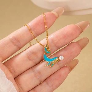 Collier dauphin doré avec émail bleu, zircons et perle porté sur la main femme