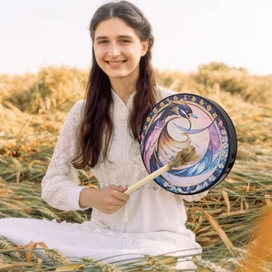 Artistic shaman drum with phoenix pattern held by a woman in a golden wheat field
