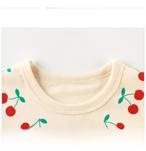 Gros plan du col rond et des motifs cerises sur ce t-shirt beige pour enfants en coton
