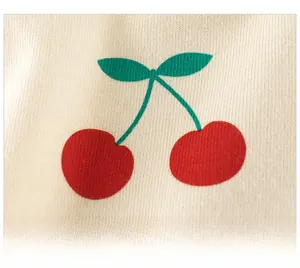 Gros plan d'une broderie de cerises rouges sur une texture de tissu en maille crème