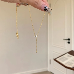 Detail of gold beaded tassel necklace featuring a sparkling clear teardrop pendant