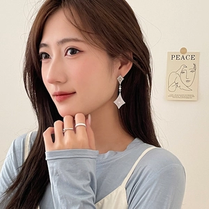 Minimalist silver diamond-shaped drop earrings and open rings set on female model