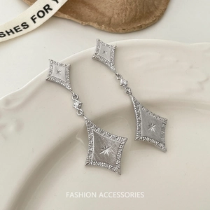 Macro shot of matte silver diamond-shaped drop earrings with brushed texture and starburst