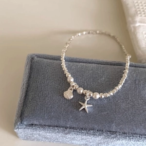 Beaded silver bracelet with starfish and shell pendants on a blue jewelry box