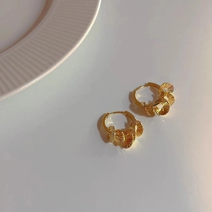 Close-up of golden hoop earrings with five fan-shaped textured metallic dangles