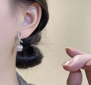 Close-up of silver knot ball earrings on a model with a polished metallic finish