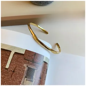 Close-up of golden irregular wavy texture bangle placed on an open book page