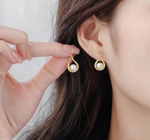 Primo piano di eleganti orecchini di perle dorate a goccia indossati per uno stile chic