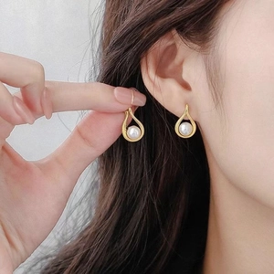 Orecchini a goccia dorati con perla indossati da una modella per un look di lusso minimale