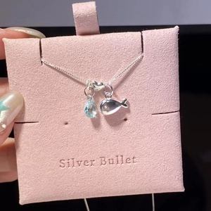 Detailed close-up of whale and blue waterdrop zircon necklace on a pink display card