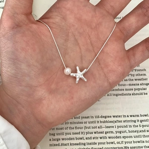 Starfish pearl necklace in silver finish shown on hand with a recipe book background