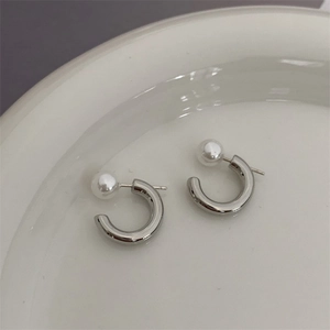 Minimalist silver C-shaped metal earrings with white pearl detail on a ceramic plate