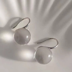 Elegant clear crystal sphere earrings with silver hooks on a wavy textured background