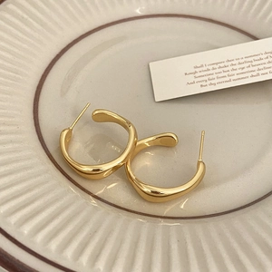 Détail de boucles d'oreilles ondulées en forme de U dorées sur un plat en céramique