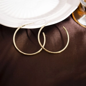 Close-up of large gold C-shaped hoop earrings on elegant brown satin with a textured finish