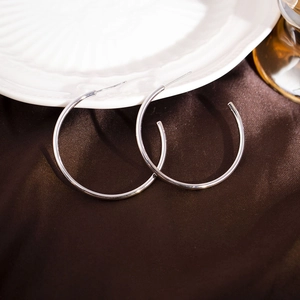Minimalist silver C-shaped hoop earrings displayed on premium brown silk background