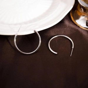 Polished silver C-shaped hoop earrings displayed on elegant silk fabric background