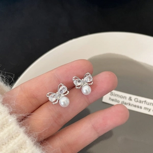 Élégantes boucles d'oreilles nœud argenté avec cristaux et perles sur une assiette blanche