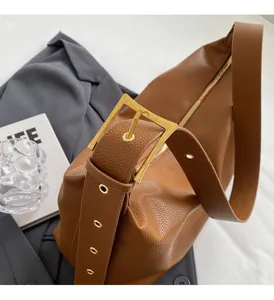 Detail of adjustable wide strap with large gold metal buckle on brown leather tote bag