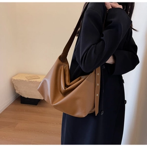 Side view of a brown pebbled leather tote bag worn by a model in a minimalist room