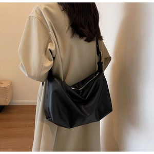 Close-up of black lychee grain leather hobo bag with adjustable strap on light trench coat