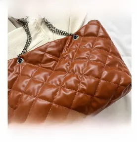 Detalle del bolso tote acolchado marrón con textura de rombos y correa de cadena