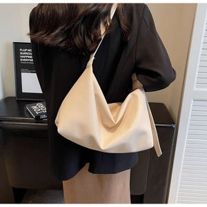 Detailed view of beige pebble leather tote bag texture and wide strap on black blazer