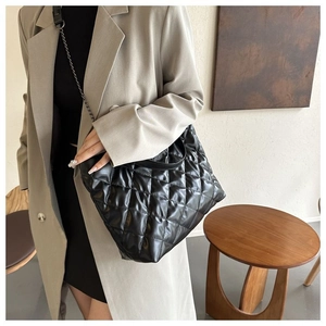 Detalle de bolso shopper acolchado negro con correa de cadena llevado por modelo