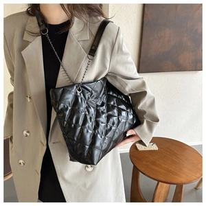 Detalle de bolso tote acolchado negro con correa de cadena y acabado en cuero brillante