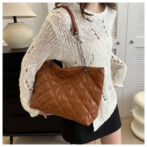 Detalle de bolso tote acolchado de cuero sintético marrón con cadena sobre una modelo