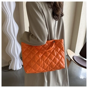 Vista detallada del bolso tote acolchado naranja con cadena y asa de cuero en modelo