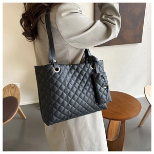 Detail of black quilted tote bag with matching pouch shown on shoulder in a cafe