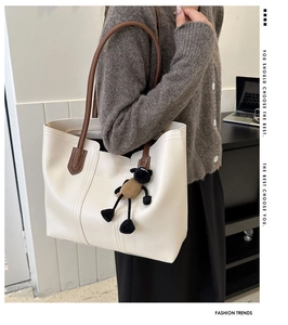 Detail showing creamy white tote bag with brown straps and cute sheep pendant on model