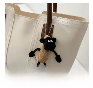 Close-up of a cute plush sheep charm in khaki and black hanging on a white tote bag handle