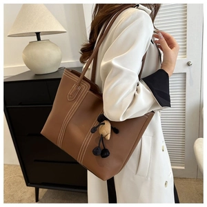 Macro shot of brown leather tote bag with white stitching detail and a plush bear charm