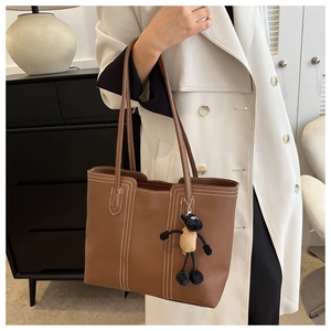 Detail of a brown leather tote bag with white contrast stitching and a cute sheep charm