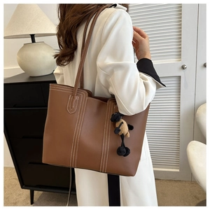 Detailed view of brown tote bag with white stitching and cute lamb charm accessory