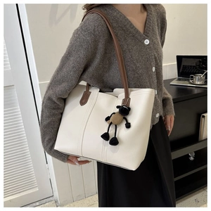Close-up of white leather tote bag with brown straps and cute black sheep plush charm