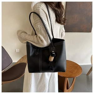 Detail of black leather tote bag with white stitching and cute sheep charm on model