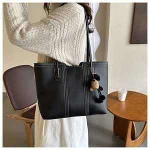 Close-up of black leather tote bag featuring white contrast stitching and a plush sheep charm